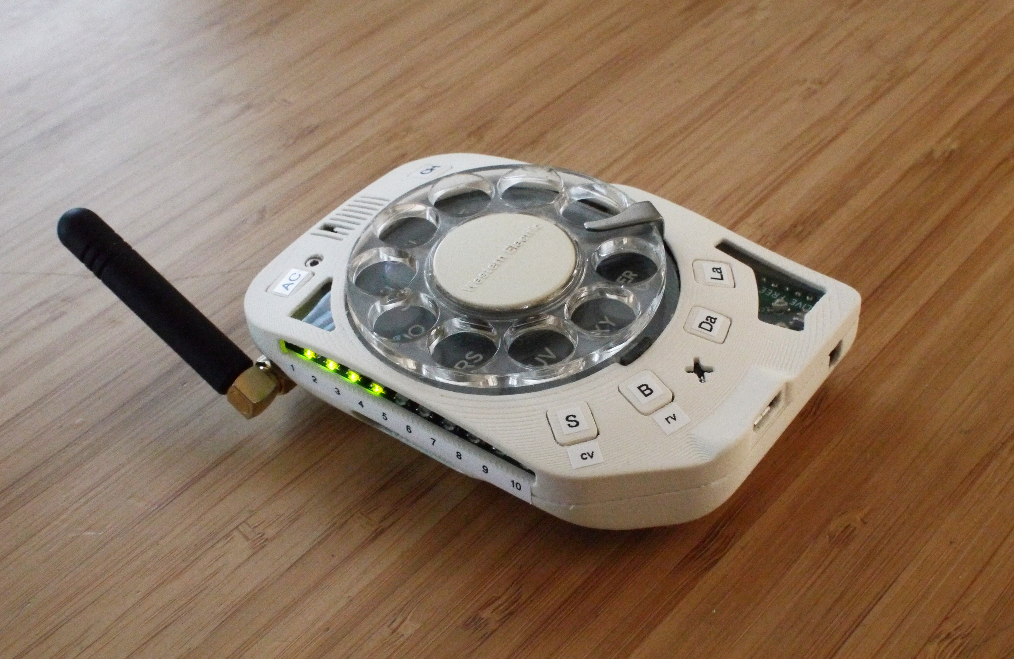 A custom-made palm-sized device with a rotary telephone dial taking up most of the front face, and various buttons and LEDs surrounding. A stubby, articulated arial comes off at one side.